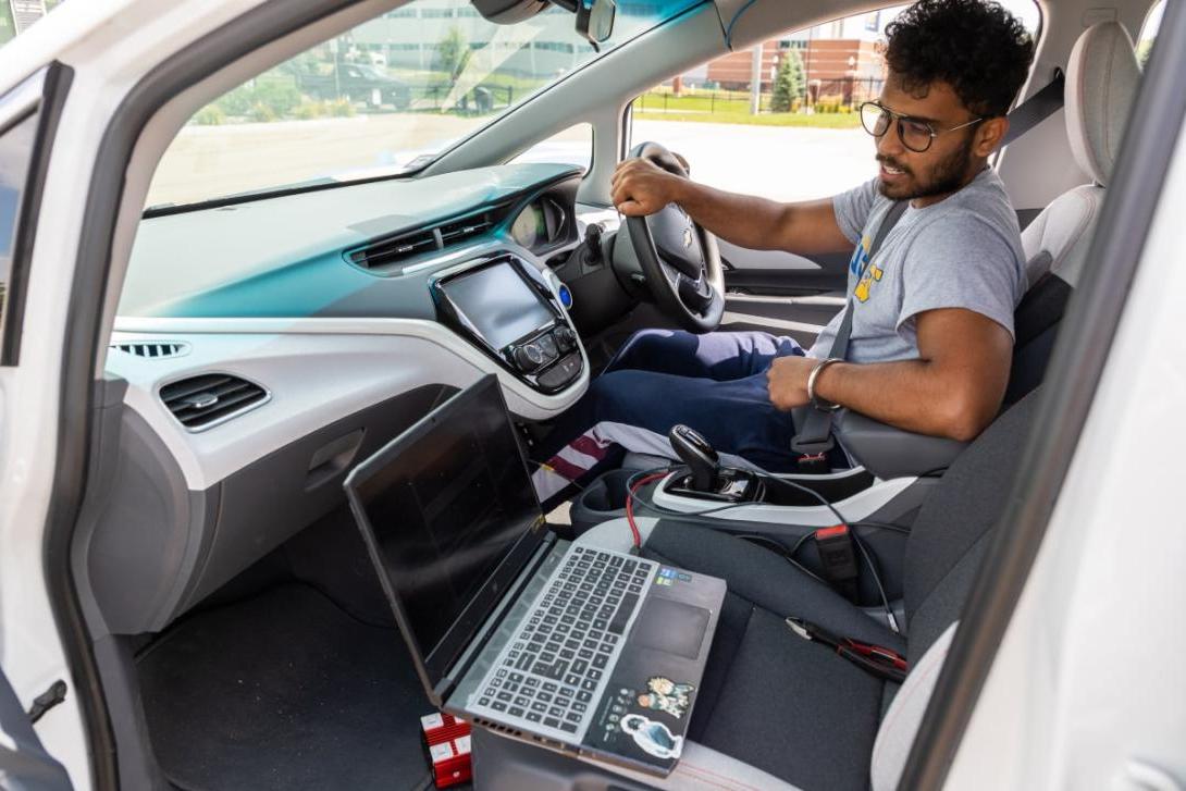 A Kettering graduate student sitting in a car reads the output from the car's computer via a laptop on the passenger seat.